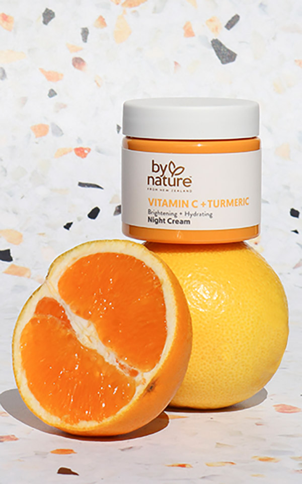 Photo of By Nature night cream in a glass jar. The jar is sitting atop a lemon, with an orange sliced in half sitting in the foreground.